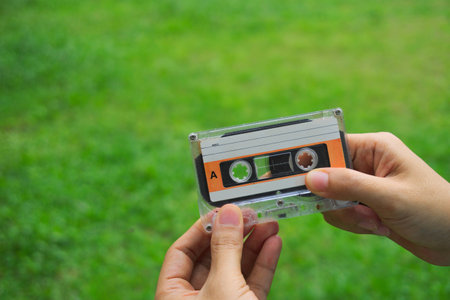 The hand is caught the cassette tape over the backdrop is grass.の写真素材