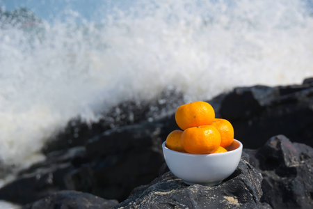 The oranges placed on the rocks and the wave splash hit rocks sea scattered as a backdrop.の写真素材