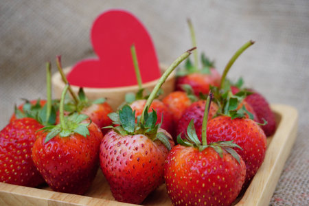 Many strawberry is placed in a tray and a paper heart in the background.の写真素材