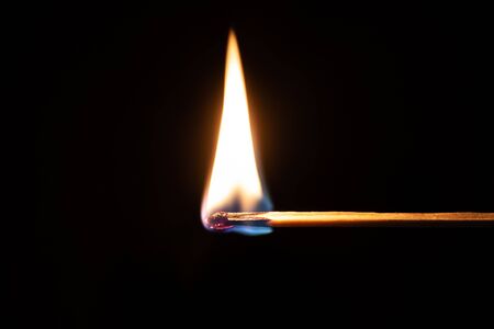 Safety match burns in front of isolated dark black backgroundの写真素材