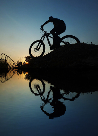 A man riding a bicycle silhouette Sunset reflections of riverの写真素材