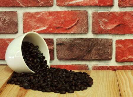 The white coffee cups fell over and coffee beans spilled on the wooden floor near the brick walls.