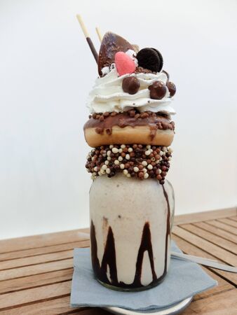 Freakshake, a kind of gourmet Milkshake with topping: donut, whipped cream, chocolate ball, wafer biscuits, candy, mikado, mini ice cream cakeの写真素材