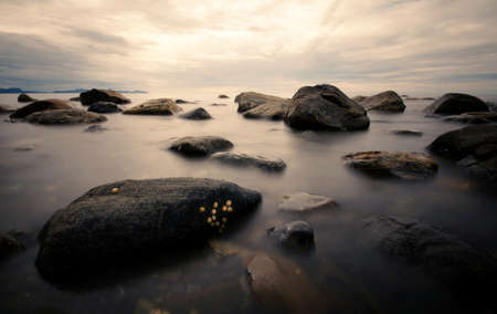 calm sea with stones during sunrise or sunset, long exposure shot of rocks in the smooth waterの写真素材