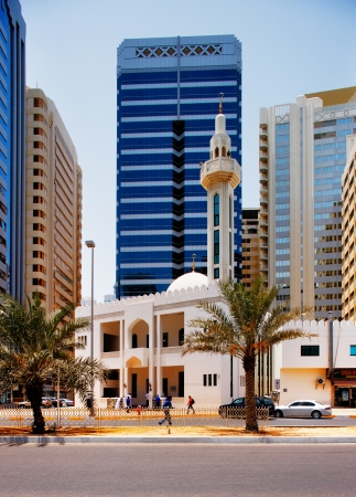 The contrast in architecture of Abu Dhabi, shows a contemporary skyscraper towering over a traditional mosqueのeditorial素材