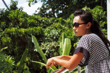 Young woman in sunglasses standing on a balcony and enjoying the viewの写真素材