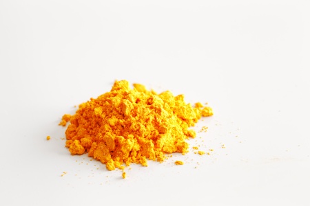 A macro image of the contents of a single turmeric capsule on white reflective ceramic surface