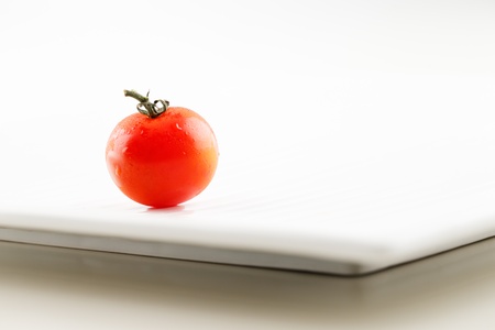 A fresh organic tomato with water droplets on a white ceramic plateの写真素材