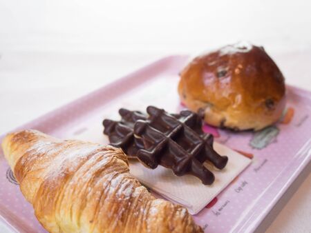 Croissant, chocolate waffle and chocolate chips bun on a pink plateの写真素材