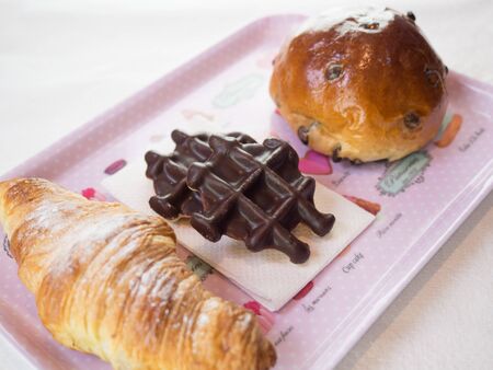 Croissant, chocolate waffle and chocolate chips bun on a pink plateの写真素材