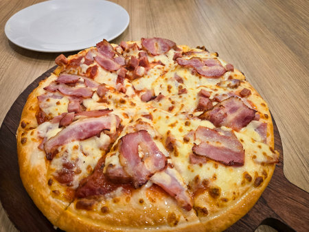 Thick crust pizza top with cubed ham, bacon and cheese on a wooden boardの写真素材