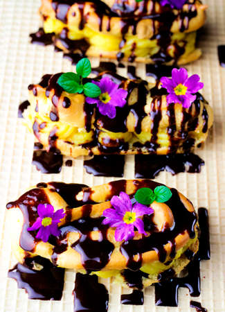 Eclairs stuffed with rich, creamy Vanilla Pastry Cream. Decorated with flowers and covered with chocolate. Spring composition. French cuisine.の写真素材