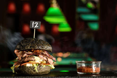 Black burger with bacon, beef, cheese, onion lettuce, tomato and sauce served on a gray stone board in the billiard lounge. Delicious meal. American cuisine.の写真素材