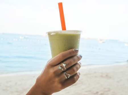 Female's hand holding multi-fruit Guava smoothie with tropical sea view background. Heaven on earth.の写真素材