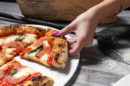 A woman enjoys a fresh Margarita Pizza straight from the wood-fired oven. Close-up of pizzas and gourmet hands. Italian cuisine. Rustic style. Culinary and restaurant concept.の写真素材