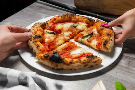 A woman and a man enjoy a fresh Margarita Pizza straight from the wood-fired oven. Close-up of pizzas and gourmet hands. Italian cuisine. Rustic style. Culinary and restaurant concept.の写真素材