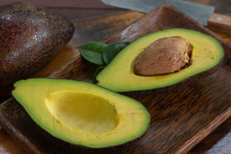 Freshly sliced Hass avocado halves lying on a tray and chopping board made of palm and teak wood....