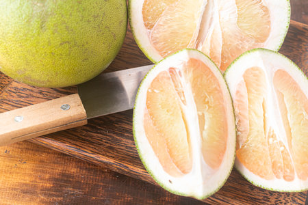 Whole Pomelo fruit (Citrus maxima) and its halves and quarters cut on a palm wood tray set against a teak cutting board. Healthy organic food, nutrition and lifestyle. Close-up.の写真素材