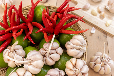 Chili peppers, limes and whole heads of garlic in a basket in the foreground, garlic in the background - Peeled garlic cloves and whole garlic on a chopping board and in a basket.の写真素材