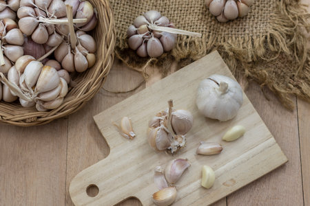 Peeled garlic cloves and whole garlic heads on a cutting board and in woven basket and on table with burlap decoration. Isolated on a beige-brown background. Healthy lifestyle.の写真素材
