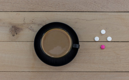 A cup of coffee on a wooden table next to painkillers and antibiotics as a symbol of the absolute non-combination of caffeine with drugs. Close-up. Macro. Interior.の写真素材