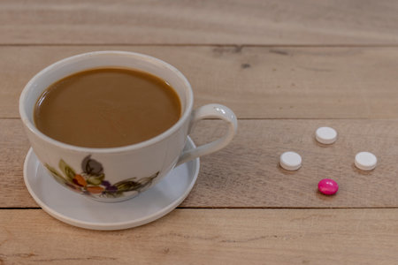 A cup of coffee on a wooden table next to painkillers and antibiotics as a symbol of the absolute non-combination of caffeine with drugs. Close-up. Macro. Interior.の写真素材