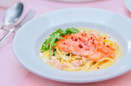 Pan Fried Salmon and Spaghetti with Cream Sauce garnished with fresh arugula. Isolated on a pink background. Close-up. Interior. Macro. Italian cuisine. Delicious meal.の写真素材