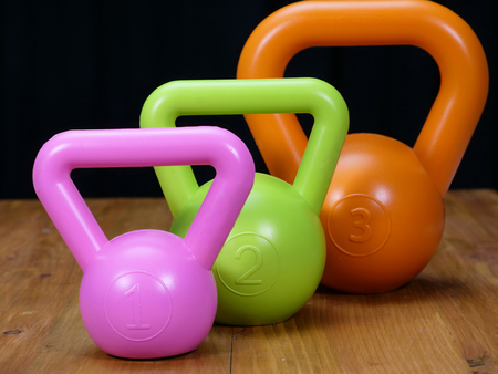 three kettle bells, pink, green, and orange, on a wooden floorの写真素材
