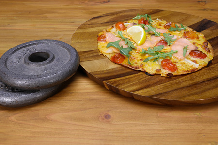 two weight plates and a salmon tomatoes pizza on a wooden tableの写真素材