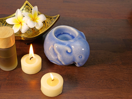 two candles, a gold pattern dish, a bottle of aromatherpy, a blue aromatherapy warmer, with white tropical flowers on a dark wood backgroundの写真素材