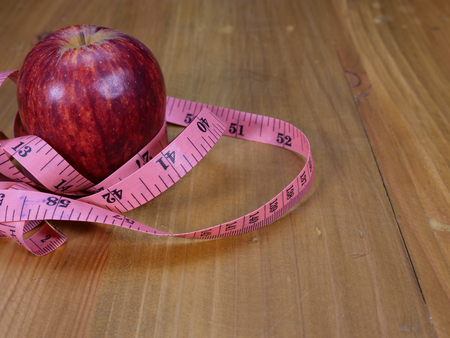 a bright red apple and a pink measuring tape on wood backgroundの写真素材