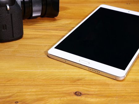 a digital camera and a tablet/smartphone on a wooden desk, conceptualizing a use of wireless digital data communicationの写真素材