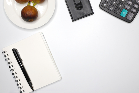 high angle view of a clean business desk top showing  a notebook, a black calculator, a black pen, a black wallet, and a fruit plateの写真素材