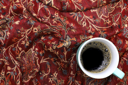 a green coffee mug with black coffee, on red and gold cotton cloth background