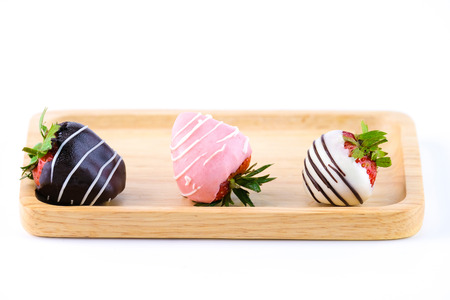 three chocolate coated strawberries (dark, pink and white) on a wooden tray, isolated on white backgroundの写真素材
