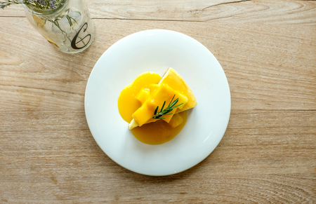 mango cheesecake with fresh mango cubes and sweet mango castade topping and rosemary sprig, profile view, closeup, on wooden backgroundの写真素材