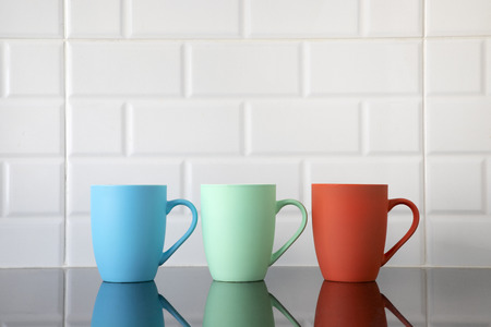 Colorful coffee mugs on black granite kitchen table with their reflections on top of the counter's...