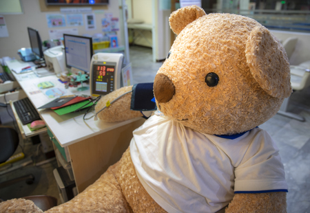 A cute live size stuffed toy bear sitting the clinic screening area having blood pressure measured.の写真素材
