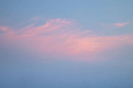 Blue sky and pink clouds  catching the reflection of sunlight at dusk. Blurred sky background.