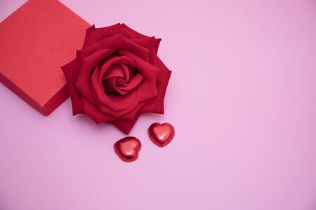 Closeup of a red rose with two chocolate candy hearts and a red gift box on pink background.  Valentine's,  anniversary, wedding concept.の写真素材