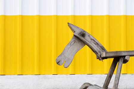 An old  wooden pony in front of a white and yellow galvanized steel wall.の写真素材