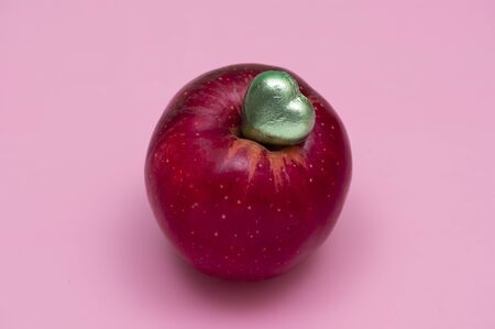 A red gala apple and a piece of chocolate candy in green foil.