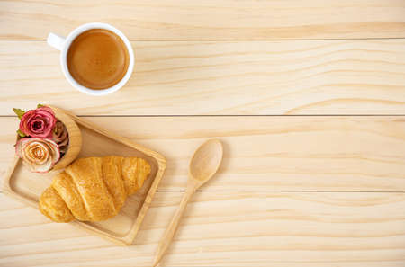 A piece of butter croissant on a squate wooden plate and a cup of coffee in white ceramic mug....
