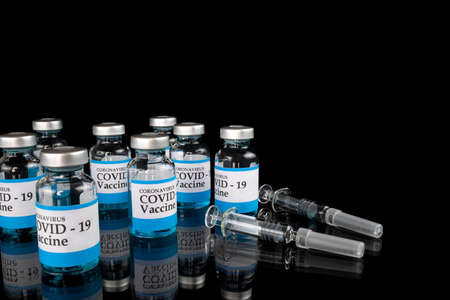 Glass vials labelled with COVID-19 text and glass syringes on black background. Covid-19 vaccination concept.の写真素材