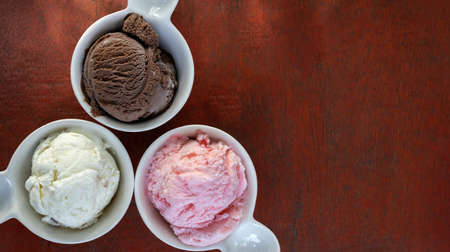 Scoops of different flavors of ice cream, vanilla, chocolate, and strawberry in small white ceramic...