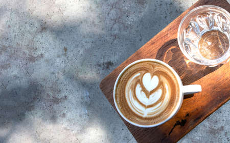 A cup of coffee and a glass of water on a concrete table under a shade of a tree.の写真素材
