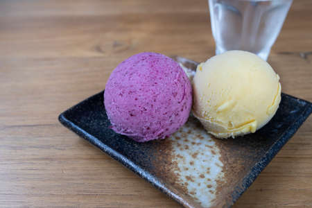 Two scoops of homemade ice cream, one made of tropical fruits from Syzygium tree or makiang in purple color and another one with vanilla flavor in creamy yellow color.の写真素材