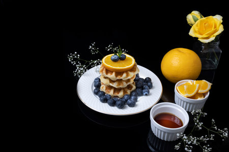 Breakfast table consisting of waffles with honey, blueberries and orange.の写真素材