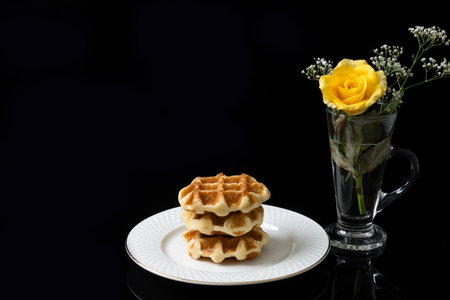 Breakfast table consisting of a stack of golden waffles and a yellow rose.の写真素材