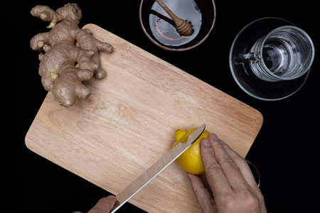 Cutting some lemon on a wooden board with ginger root and a cup of honey. Preparing lemon honey ginger herbal tea concepts.の写真素材